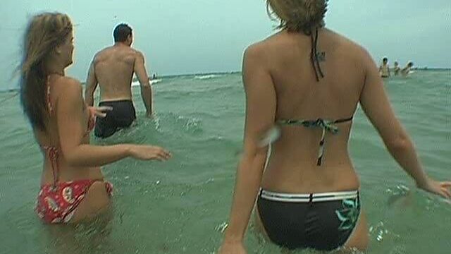 Two alluring students swim in ocean with a brutal dude